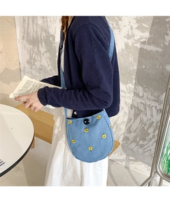 Gros plan détaillé du sac bandoulière en toile bleue avec motifs brodés floraux jaunes