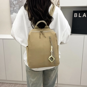 Detail of khaki nylon backpack featuring a side zipper pocket and a letter M pendant tag