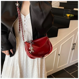 Close-up of red patent leather crossbody bag with silver bear charm and metal chain strap