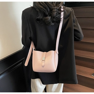 Gros plan d'un sac seau rose en cuir grainé porté avec une tenue de blazer noir