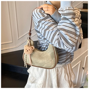 Detail of khaki crescent shoulder bag featuring a brown plush bear charm and matte leather finish