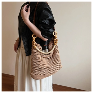 Detail of woven beach bag featuring a round wooden handle and brown leather shoulder strap