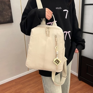 Detail view of large beige nylon backpack with side pockets and a stylish m-shaped pendant