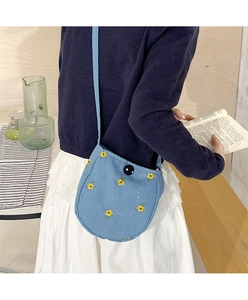 Détail du sac bandoulière en coton bleu clair avec broderie florale jaune et bouton décoratif