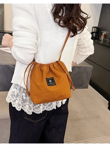 Chic drawstring bucket bag in vibrant orange canvas with sleek leather crossbody strap