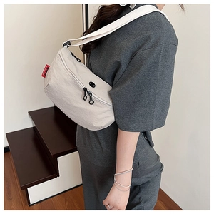 Detailed shot of an off-white casual crossbody bag with double zippers and red side tag
