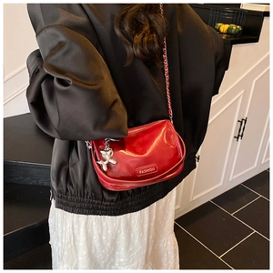 Detail of red patent leather crossbody bag with silver chain and balloon dog charm on a model