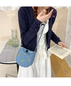 Détail du sac à bandoulière en denim bleu avec broderie florale et boucle noire ronde