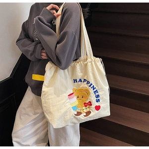 Detail of canvas tote bag showing bear embroidery, blue text, and yellow drawstring straps
