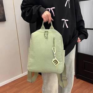 Detail of light green textured nylon backpack with vertical zipper and decorative M pendant
