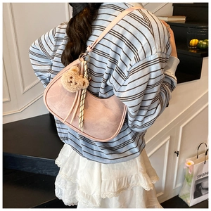 Detail view of a pink hobo underarm bag with a plush bear charm and striped ribbon strap