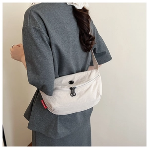 Detail view of beige nylon crossbody dumpling bag featuring black zipper and round logo