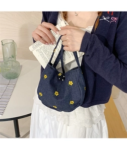 Gros plan détaillé du sac en jean bleu foncé avec broderies florales jaunes et bouton à pois