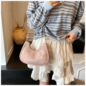 Pink suede-like crescent underarm bag worn by a model with a casual street style look