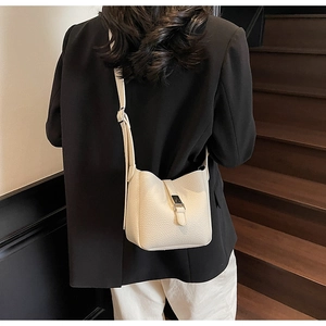 Minimalist beige pebble leather bucket bag styled on model with silver metal buckle detail