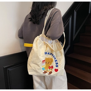 Detail of beige canvas tote bag with drawstring closure and blue teddy bear embroidery