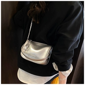 Silver metallic saddle bag with chain strap and butterfly charm worn over a black hoodie