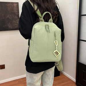 Detail of light green nylon backpack featuring functional pockets and an 'm' letter charm