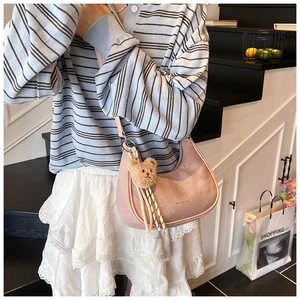 Pink crescent underarm bag with plush bear charm and woven tassel details on stairs