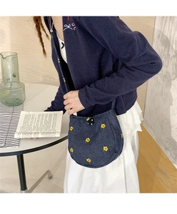 Gros plan d'un sac bandoulière en denim bleu avec broderie florale jaune et bouton à pois