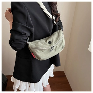 Detail of light green nylon crescent crossbody bag with double zippers and red side tag
