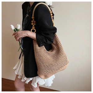 Close-up of woven straw tote bag featuring decorative wooden bead and ring shoulder straps