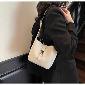 Sac seau crème à texture litchi porté comme un élégant sac à bandoulière sous le bras