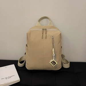 Detail of khaki nylon backpack featuring vertical zipper pocket and M letter pendant