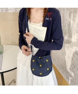 Détail d'un sac bandoulière en denim bleu avec broderies fleurs jaunes sur robe dentelle