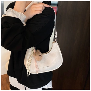 Detail view of a white crescent underarm bag with a cute brown plush bear charm