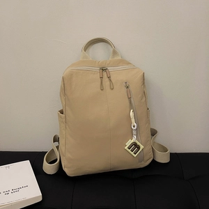 Close-up of beige minimalist backpack featuring vertical zipper and letter m charm