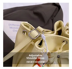 Close-up of drawstring closure and adjustable strap on cream bucket bag with doll charm