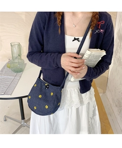 Gros plan du petit sac bandoulière en toile bleu foncé avec broderie florale jaune et bouton