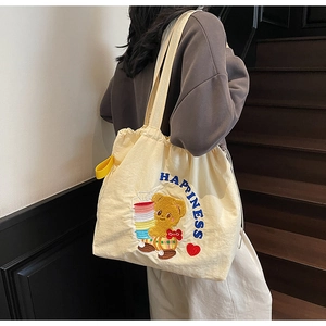 Close-up of a beige tote bag with a cartoon bear embroidery and blue HAPPINESS lettering