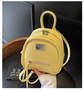 Detail of a bright yellow mini backpack in smooth PU leather with silver metal logo plate