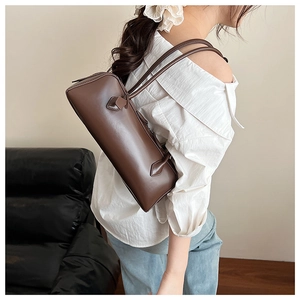 Deep brown leather baguette bag with dual slim straps shown on a model's shoulder