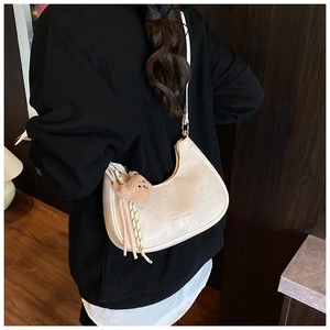 Detail of ivory crescent shoulder bag featuring a plush bear charm and woven rope accent