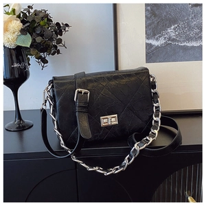 Close-up of black quilted leather shoulder bag with silver chain on modern cabinet