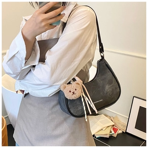 Detail of black faux leather crescent bag with plush bear charm and ribbon accent