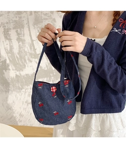 Détail d'un sac bandoulière en denim bleu avec broderie cerise et bouton à carreaux