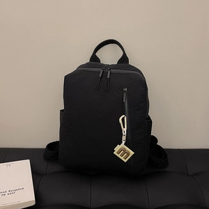 Detail of black nylon backpack featuring smooth texture and cream letter charm