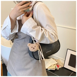 Detail of black crescent moon shoulder bag featuring cute bear charm and striped silk scarf