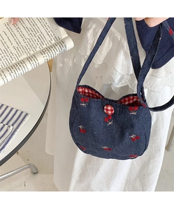 Détail du sac à bandoulière en denim avec broderie cerise et fermeture à bouton à carreaux