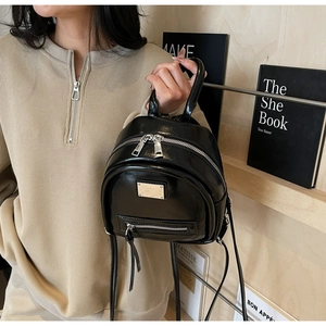 Detail view of a black glossy mini backpack with metal plaque and multi-pocket design