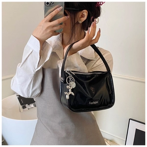 Detail of glossy black patent leather handbag featuring silver Fashion plaque and balloon dog charm