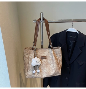Détail d'un sac cabas fleuri kaki avec lanières en cuir et breloque nuage en peluche