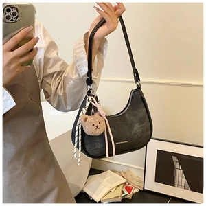 Detail of black crescent shoulder bag with golden zipper and plush bear charm
