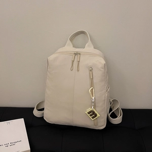 Detail of a cream nylon backpack with wide handles, dual zippers, and 'm' charm on a bench