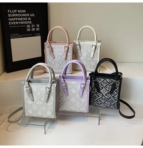 Détail de sacs bandoulière tissés colorés à motif floral sur un présentoir blanc