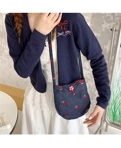 Détail du sac bandoulière en jean avec broderie cerise et bouton à carreaux rouges